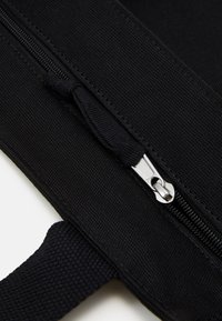 Svart tygväska med en strukturerad yta, utrustad med en silverfärgad dragkedja och ett vävt handtag, designad för hållbarhet och praktisk användning.