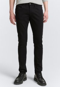 Jeans de algodón negro con corte slim, que cuentan con cinco bolsillos y una cremallera. La tela texturizada presenta sutiles detalles desvaídos.