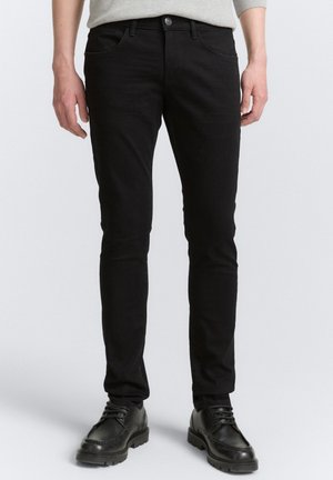 Schwarze Baumwolljeans mit schlanker Passform, die fünf Taschen und einen Reißverschluss hat. Der strukturierte Stoff weist dezente Ausbleichungen auf.