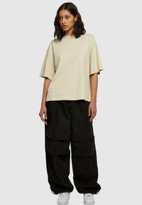 Beige oversize tričko s širokými rukávy, spárované s volnými černými cargo kalhotami s velkými kapsami a bílými teniskami.