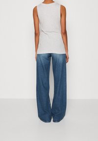 Top sin mangas de color gris claro combinado con jeans de mezclilla oscuros de pierna ancha. La tela es suave con una ligera textura; los jeans tienen un corte clásico.