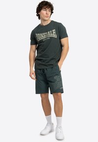 Grøn bomuld T-shirt med "LONSDALE LONDON" grafik, parret med matchende shorts med logo print, samt hvide sneakers og sokker.