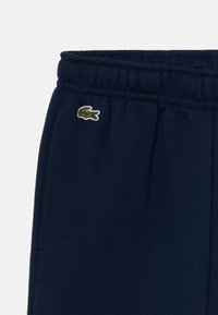 Pantalons de survêtement bleu marine avec une taille élastique, arborant un petit logo de crocodile brodé en vert à l'avant. Tissu en coton doux.