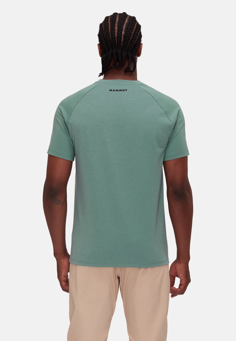Camiseta verde de manga corta con escote redondeado, que presenta un diseño sin costuras en los hombros raglán y un pequeño logo de "Mammut" en la parte trasera.