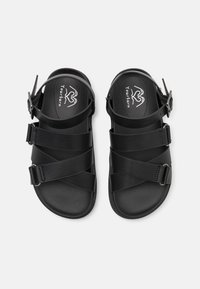 Svarta sandaler med flera remmar och en bakre hälrem. Slät material med platt sula och justerbar spänndetalj.