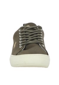 Baskets en toile vert olive avec un bout rond, semelle blanche et lacets assortis. Présente un logo sur le côté et des œillets en métal pour les lacets.