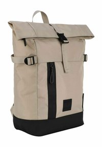 Sac à dos beige à rabat avec des accents noirs, fabriqué en tissu texturé. Il dispose de bretelles réglables, d'une poche zippée et d'un patch avec logo à l'avant.