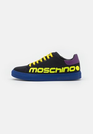 Schwarzer Low-Top-Sneaker mit blauer Sohle, gelben Schnürsenkeln, neongelbem „Moschino“-Schriftzug und lila Fersendetail, Seitenansicht vor weißem Hintergrund.