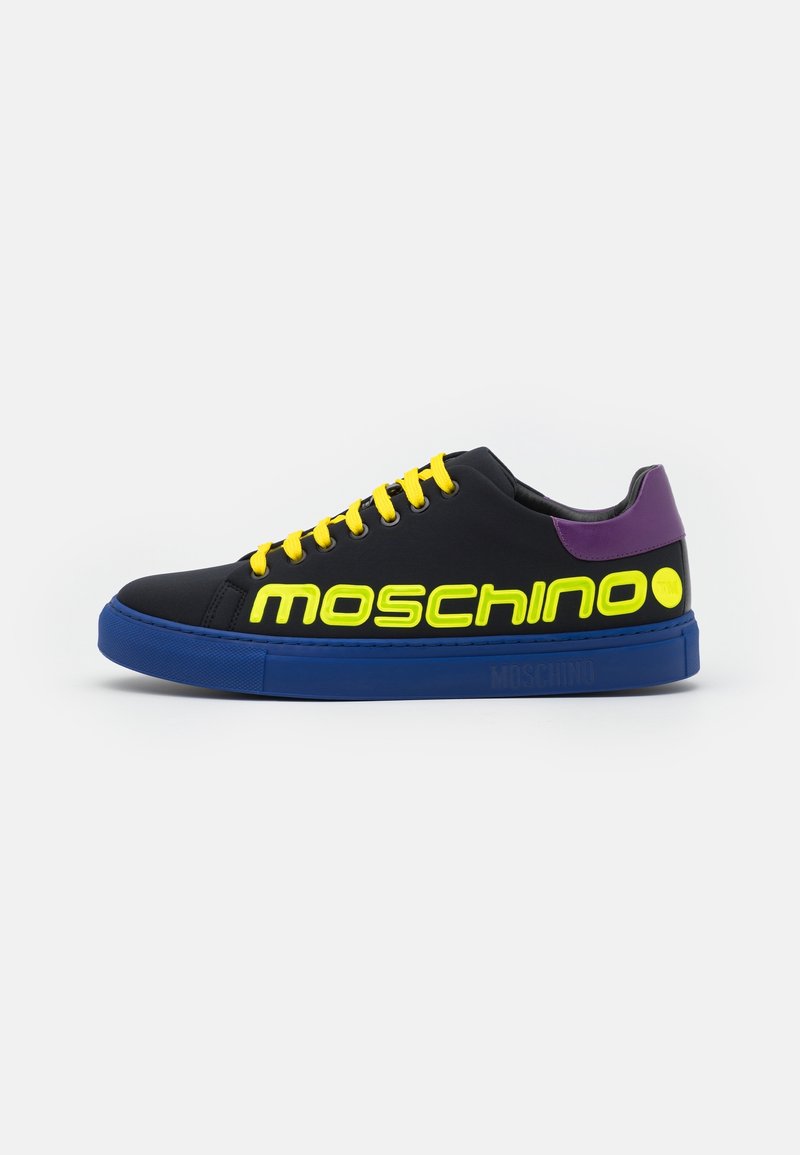Basket basse noire avec semelle bleue, lacets jaunes, texte « Moschino » jaune fluo et détail violet au talon, vue de côté sur fond blanc.