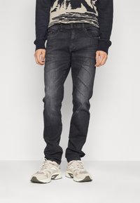 Jeans de mezclilla azul oscuro de corte slim, con bolsillos frontales, un ligero desvanecimiento y combinados con zapatillas deportivas de color claro.