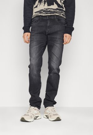 Dark blue denim jeans with a slim fit, featuring front pockets, subtle fading, and paired with light-colored athletic sneakers.