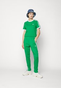 Green athletic outfit consisting of a short-sleeved shirt with white accents and matching pants with side stripes. White sneakers and a blue hat.