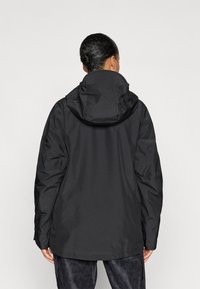 Schwarze wasserdichte Jacke mit Kapuze, entspannter Schnitt, matte Oberfläche und elastischen Bündchen. Die Rückansicht zeigt Nahtdetails und keine Verzierungen.