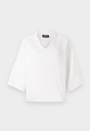 Fehér, rövid ujjú kötött felső V-nyakkal és enyhén struktúrált gallérral. Simaság jellemzi, dobozszerű forma és minimalista dizájn.