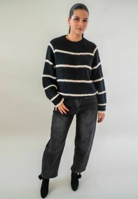 Pull en tricot noir et blanc à rayures avec des manches larges, associé à un jean noir taille haute et des bottines noires.