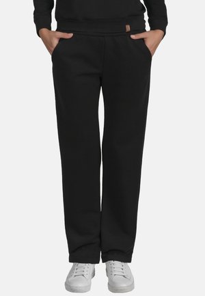 Pantalons de jogging noirs à coupe décontractée, avec taille élastique et poches latérales. Le tissu semble doux ; associés à des baskets blanches.