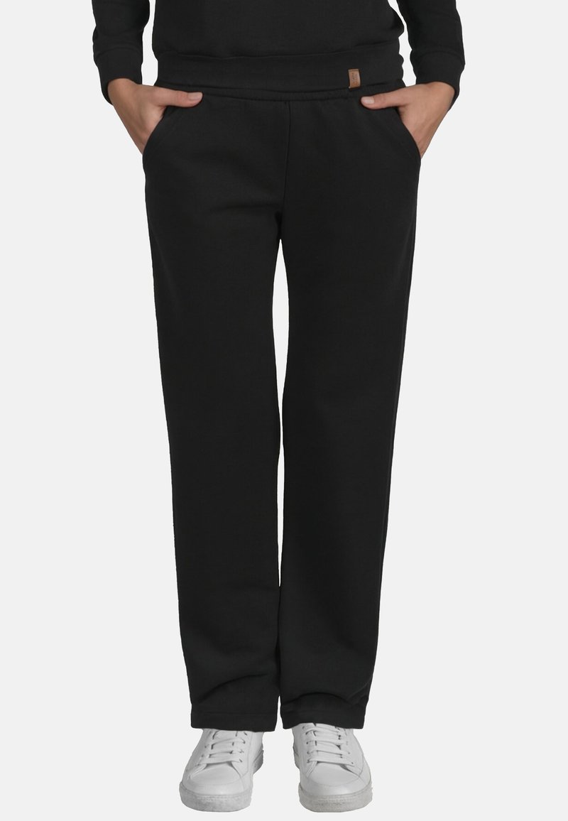 Pantalones de chándal negros con un corte relajado, cinturilla elástica y bolsillos laterales. La tela parece suave; combinados con zapatillas blancas.