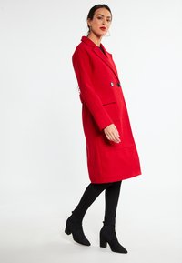 Cappotto rosso in lana con un design su misura, bottoni doppi e tasche laterali. Abbinato a leggings neri attillati e tacchi a blocco.
