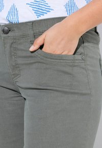 Pantalon en coton gris avec une poche latérale, des coutures plates et une texture subtile. Le tissu semble doux et durable.