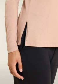 Maglietta a maniche lunghe di un rosa chiaro con fessure laterali e dettagli in rivetti argentati, abbinata a pantaloni neri scuri. Tessuto morbido con una superficie liscia.