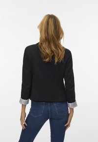 Schwarze Jacke mit Dreiviertelärmeln, die über gestreiften Bündchen verfügt. Getragen über blauen Jeans, die eine maßgeschneiderte Passform und glatte Textur zeigen.
