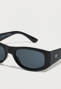 Gafas de sol negras con montura rectangular y gruesa. Lentes oscuras y detalle sutil del logo en el lateral. Acabado elegante y brillante.