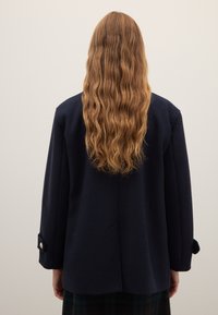 Blazer in misto lana blu navy con vestibilità rilassata, caratterizzato da uno spacco posteriore singolo, maniche lunghe e bottoni decorativi sui polsini.