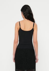 Canotta nera con spalline sottili, caratterizzata da un design aderente e una texture liscia, abbinata a una gonna in pizzo per un dettaglio aggiuntivo.