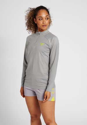 Maglia atletica grigia chiara a maniche lunghe con zip frontale e logo; abbinata a pantaloni corti grigi chiari con un motivo geometrico giallo.
