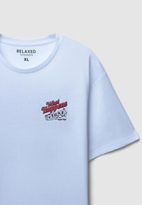 Biała bawełniana koszulka z nadrukiem graficznym, na którym znajduje się napis „Co się dzieje w VEGAS”, z kostkami do gry i kolorowym napisem na piersi.