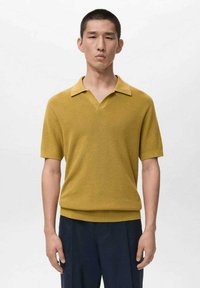 Polo a maniche corte giallo senape con scollo a V, trama a coste e colletto piatto. Abbinata a pantaloni blu scuro. Design semplice.