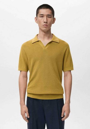 Hořčicově žluté polo tričko s krátkým rukávem a výstřihem do V, s žebrovanou texturou a plochým límcem. Kombinováno s tmavě modrými kalhotami. Jednoduchý design.