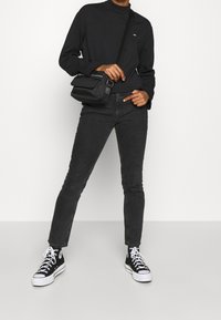 Maglietta nera a maniche lunghe, jeans slim-fit grigio scuro, e sneakers nere alte, completati da una piccola borsa a tracolla nera.
