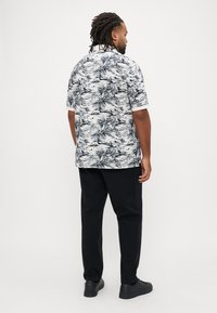 Košulja s kratkim rukavima i kopčanjem na gumbe, s uzorkom crno-bijelih palmi, uparena s crnim hlačama i crnim tenisicama.