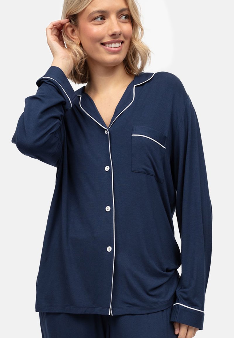 Camisa de pijama azul marino en tela suave, con cierre de botones en el frente, ribetes blancos y un solo bolsillo en el pecho, con un corte relajado.