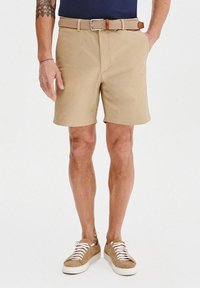 Beżowe szorty o prostym kroju, z teksturowanym brązowym paskiem. Poł�ączone z jasnobrązowymi trampkami i białymi sznurówkami.