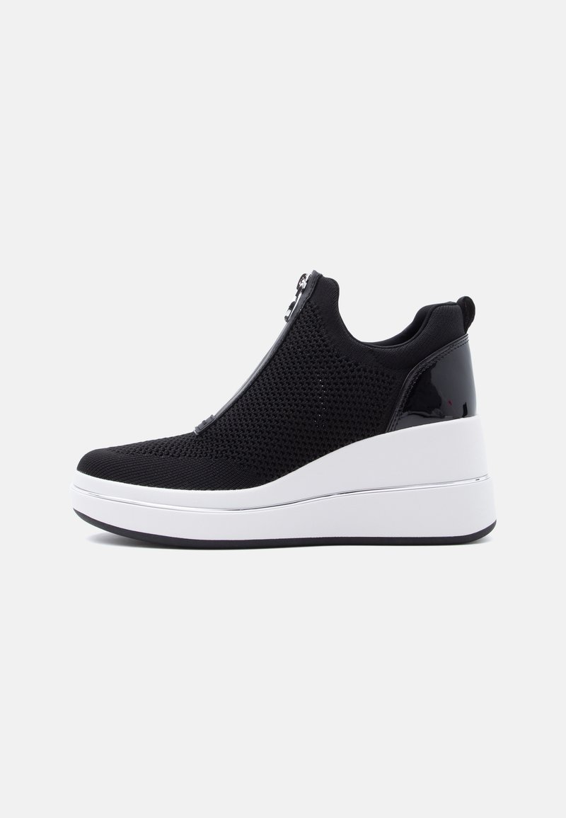 Μαύρο καλάθι πλεκτού με σφήνα και φερμουάρ στο μπροστινό μέρος, ψηλή λευκή σόλα πλατφόρμας, και γυαλιστερό μαύρο πίσω πάνελ, πλευρική άποψη σε λευκό φόντο.