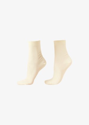 Par de calcetines tobilleros acanalados de color crema mostrados en maniquíes de pie sobre fondo blanco.