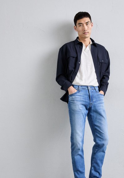 Námornícka košeľa na gombíky s dvoma náprsými vreckami, biela tričko s kruhovým výstrihom a svetlomodré džínsy. Hladká tkanina s ležérnym strihom.