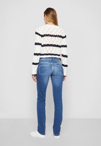 Pull en maille cropped rayé blanc et marine avec un motif en losanges, associé à un jean bleu taille mi-haute avec poches arrières et léger délavage.