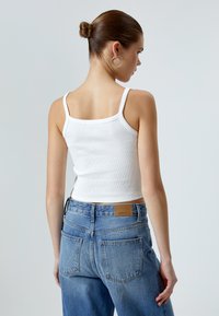 Hvid ribbet tanktop med tynde stropper, parret med lyseblå højtaljede jeans med et lædermærke og subtile falmninger i stoffet.