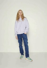 Sudadera lila claro, vaqueros azules y zapatillas multicolores. Corte informal, mangas largas y diseño de pierna holgada. Textura suave.