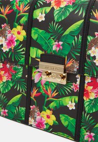 Borsa a tracolla con motivo floreale su sfondo nero, decorata con vivaci fiori tropicali, foglie verdi e una chiusura dorata con dettagli del logo.