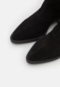 Bottines en daim noir avec un bout pointu et un design élégant. Caractérisées par une texture lisse et une semelle en caoutchouc minimaliste.