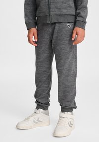 Graue sportliche Jogginghosen mit elastischen Bündchen, aus weichem Stoff. Sie verfügen über ein kleines Logo-Detail. Kombiniert mit weißen High-Top-Sneakern.