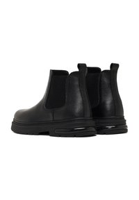 Botas Chelsea de cuero negro con paneles laterales elásticos, puntera redondeada, suela gruesa y tirador trasero. Acabado texturizado con sutiles detalles de costura.