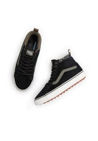 Černé vysoké tenisky z broušené kůže se zelenými akcenty, bílou gumovou podrážkou a podšívkou s maskáčovým vzorem. Disponují plochými tkaničkami a poutkem na zadní straně.