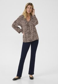 Blouse imprimée léopard avec un col en V, des manches longues et des poignets froncés, associée à un jean droit bleu foncé et des ballerines noires.