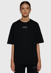 Svart oversized t-shirt i bomull med rund halsringning. Har en framlogotyp "HALO" tryckt i guld. Kort ärm med avslappnad passform.