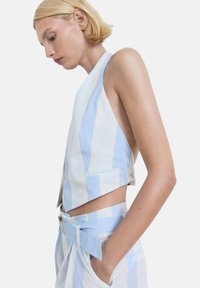 Prugasta brezrokavna majica v svetlo modri in beli barvi iz bombaža, z obrezanim krojem in stranskimi žepi, v kombinaciji z usklajenimi hlačami s pasom.